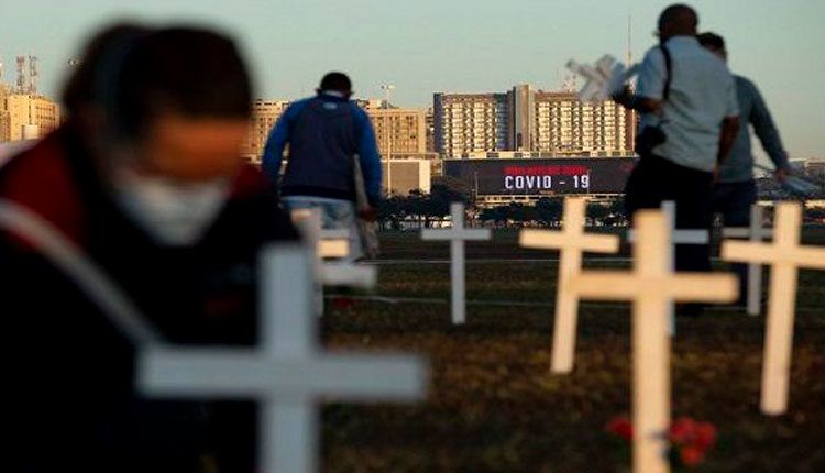 Varias personas participan en las instalación de centenares de cruces como homenaje a las víctimas de COVID-19 este domingo, en la Explanada de los Ministerios de Brasil, en Brasilia. Foto: EFE.